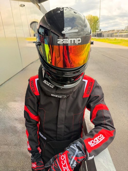 Driver in a black and red racing suit with a mirrored helmet