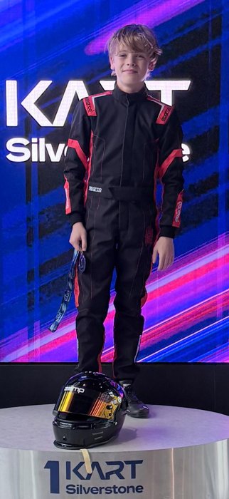 Driver in a black and red suit holding medals on the podium